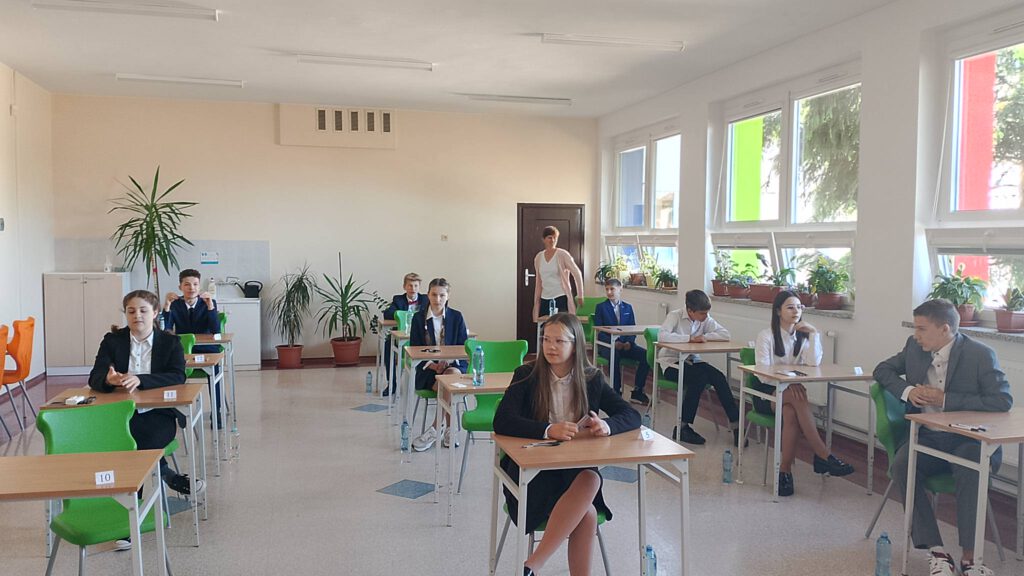 Egzamin ósmoklasisty. Na zdjęciu uczniowie klasy ósmej ubrani na galowo siedzą w sali i czekają na rozpoczęcie egzaminu.  