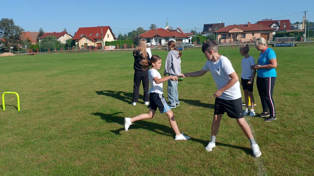 Ogórkowa sztafeta- szkolna akcja sportowa. Na zdjęciu uczniowie podczas biegu, dziewczynka przekazuje chłopcu pałeczkę. 