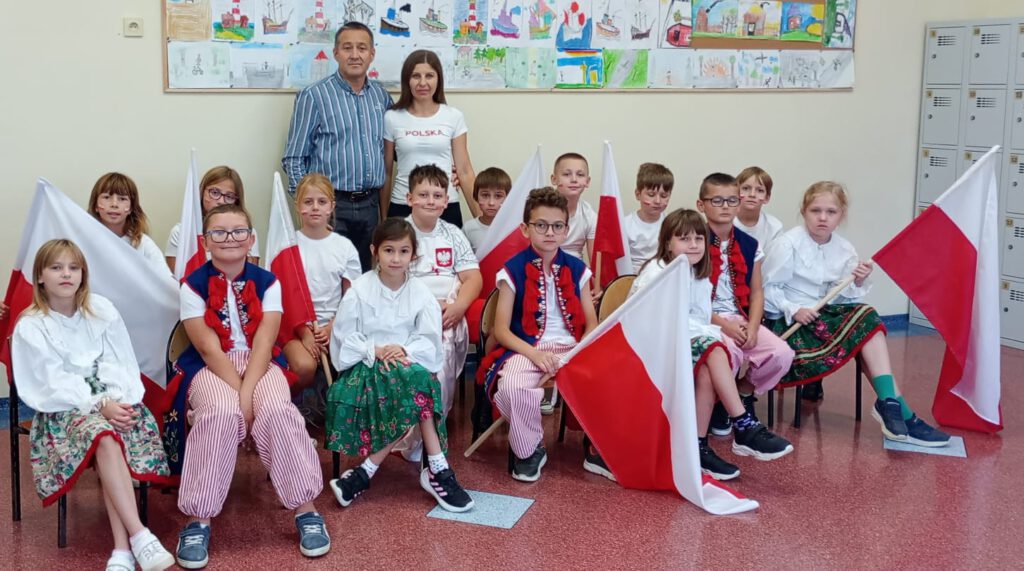 Projekt #Active Sister Schools. Na zdjęciu uczniowie klasy trzeciej b ubrani w biało-czerwone stroje trzymając biało-czerwone flagi pozują do zdjęcia klasowego. 