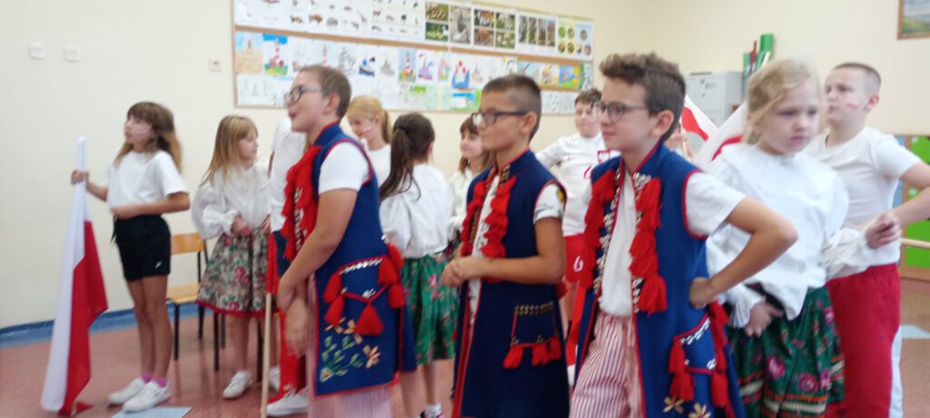 Projekt #Active Sister Schools. Na zdjęciu uczniowie klasy trzeciej b ubrani w biało-czerwone stroje i stroje ludowe czekają na wyniki losowania składu drużyn  w projekcie. 