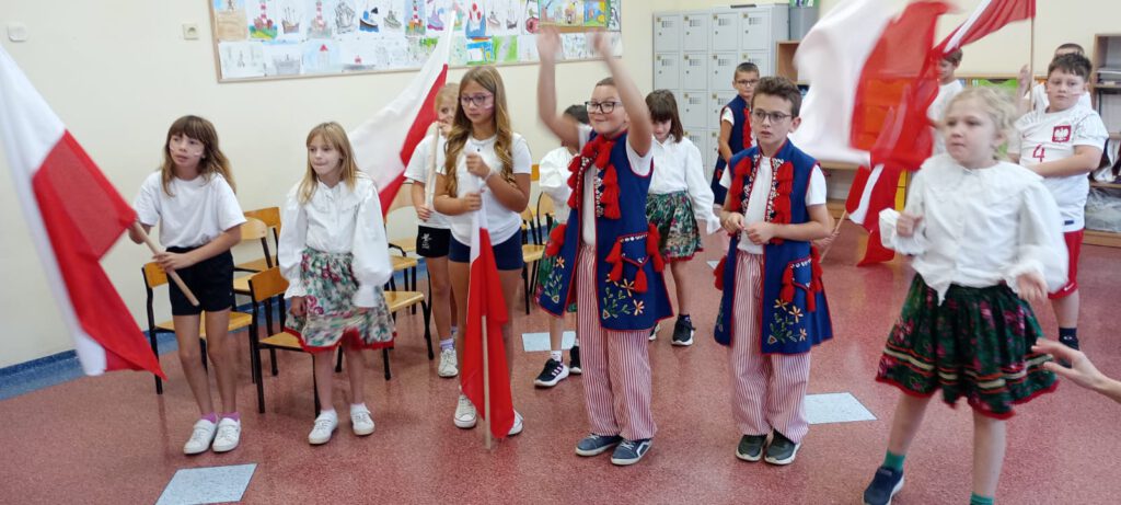 Projekt #Active Sister Schools. Na zdjęciu uczniowie klasy trzeciej b ubrani w biało-czerwone stroje i stroje ludowe cieszą się z losowania drużyn w projekcie. 