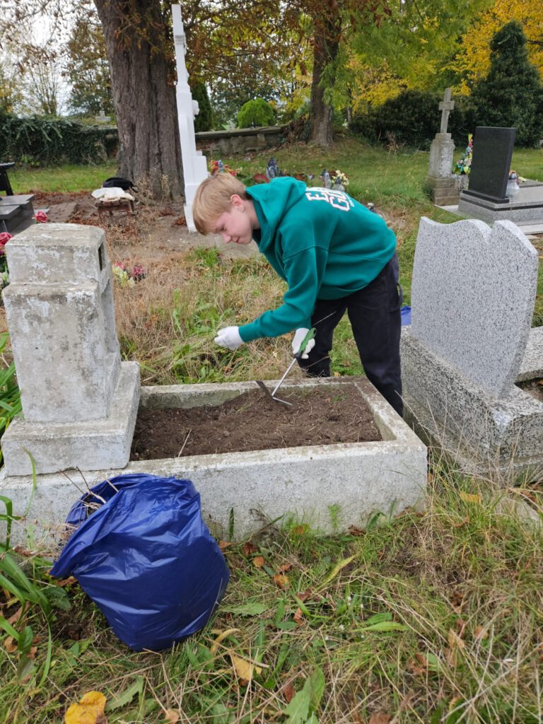 Na zdjęciu uczniowie  zajmują się porządkowaniem zaniedbanych grobów. Wyrywają trawę i usuwają stare kwiaty i znicze.