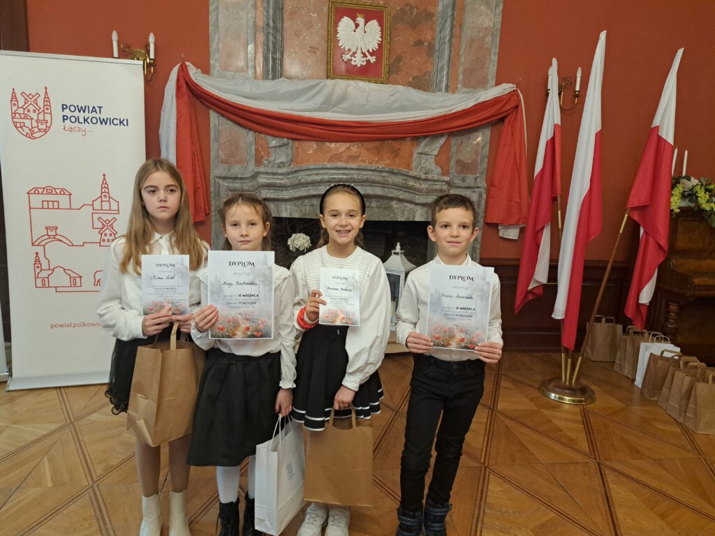 Przedstawia uczestników naszej szkoły w konkursie "(Młode) Pokolenie". Uczniowie ubrani są w strój galowy, czyli biała bluzka i czarna spodniczka lub czarne spodnie.  W tle zdjęcia widać kominek z godłem Polski oraz przywieszone biało-czerwone flagi. 