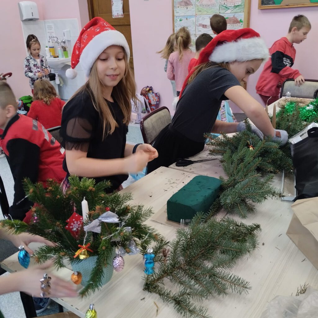 Przygotowania do świąt- stroiki świąteczne. Uczennice z klasy 2a wbijają świerkowe gałązki w gąbki florystyczne, nadając stroikowi odpowiedni kształt.