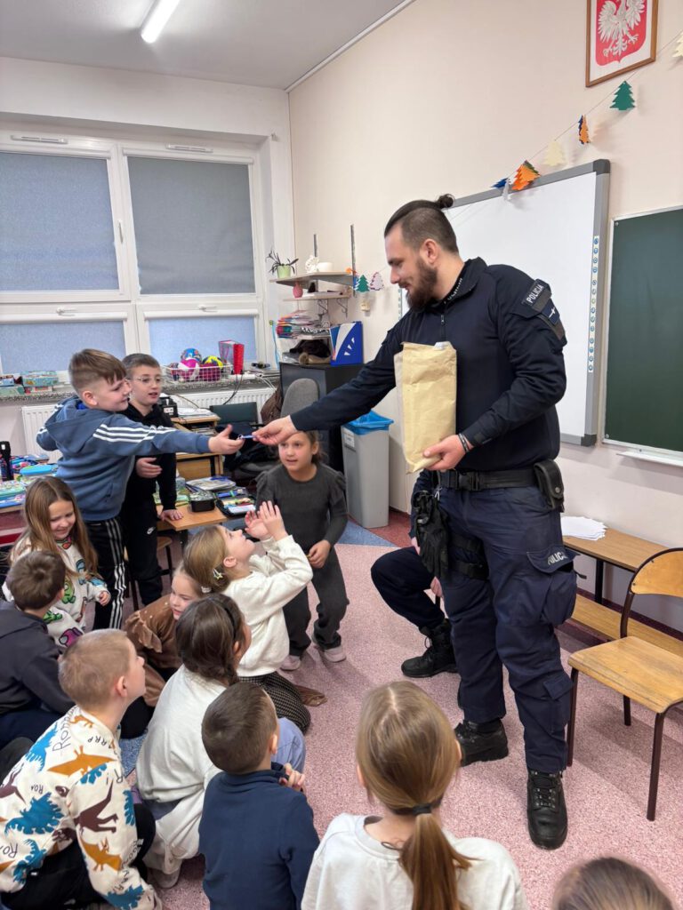 Prelekcja "Bezpieczne ferie". na zdjęciu policjant rozdaje dzieciom odblaski. 