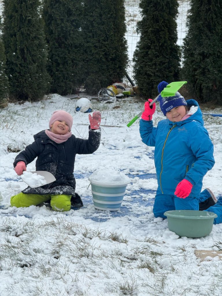 Moving Schools Challenger – przegląd stycznia. Na zdjęciu dwie  uczennice bawią się na śniegu, ładują śnieg do wiaderka łopatkami. 