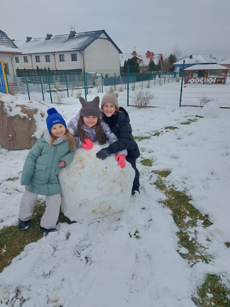 Moving Schools Challenger – przegląd stycznia. Na zdjęciu trzy uśmiechnięte uczennice  bawią się na śniegu, opierają się o dużą kulę śniegu. 