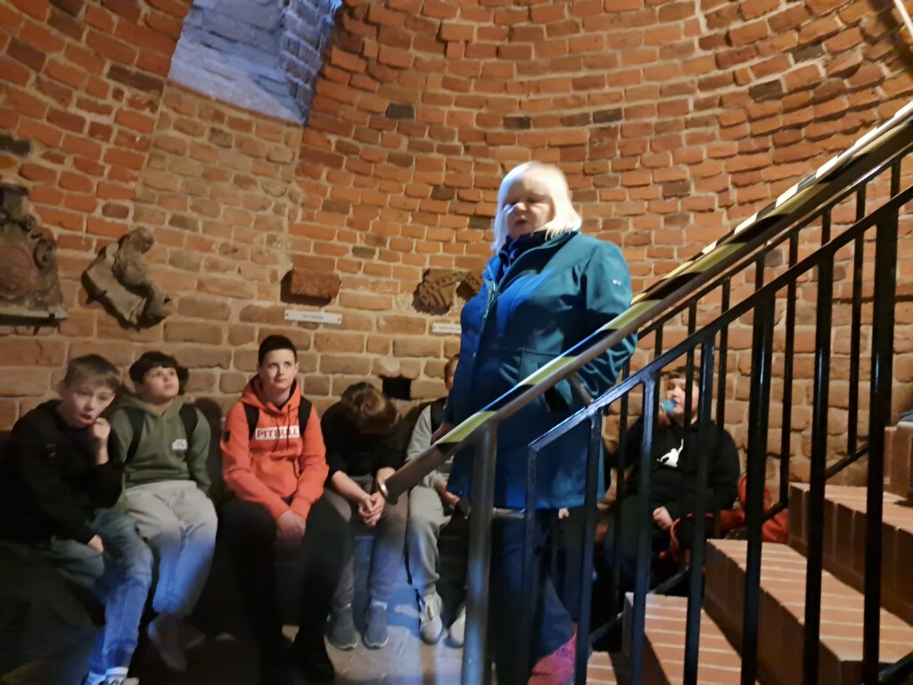 Przedstawia uśmiechnięte uczennic na szczycie wieży głogowskiego zamku. W tle zdjęcia przepiękna panorama na miasto Głogów.