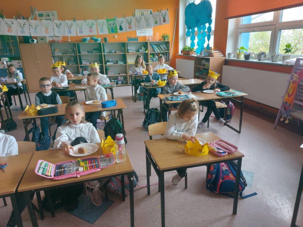 Tysiąclecie koronacji Bolesława I Chrobrego. Na zdjęciu uczniowie klasy pierwszej siedzą przy ławeczkach i jedzą szarlotką.
