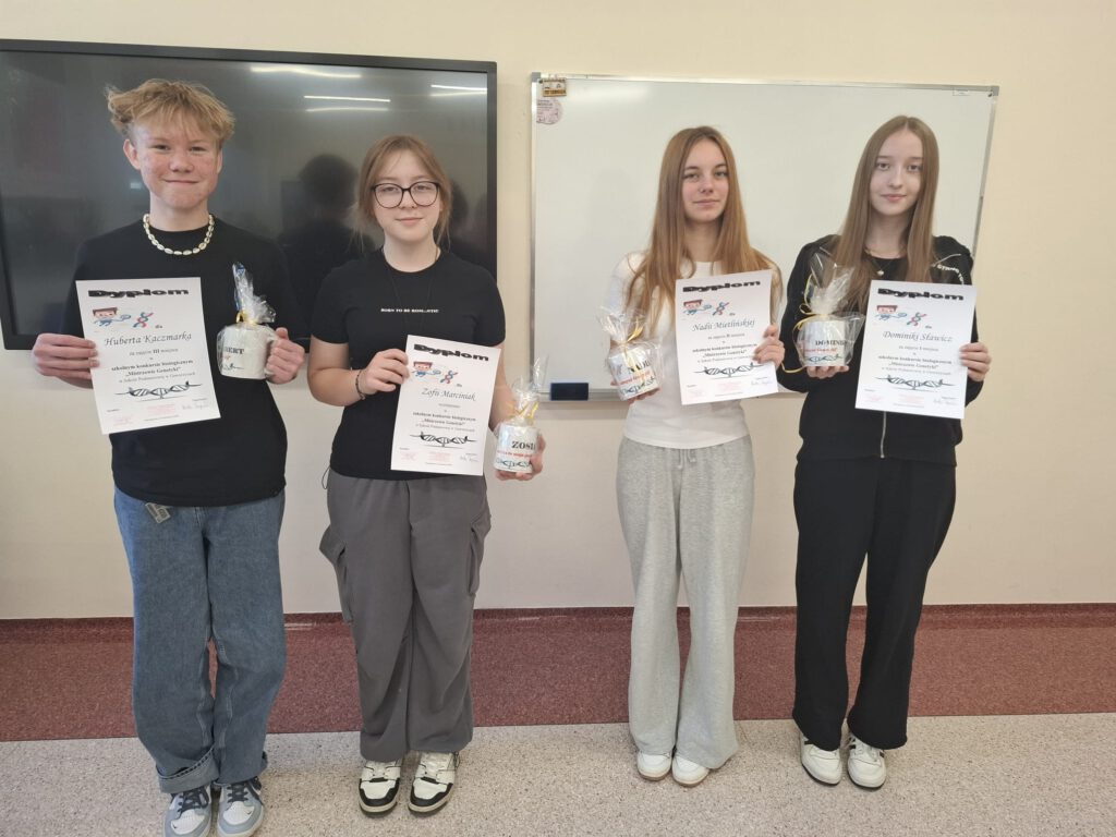 Zdjęcie nr 1 przedstawia laureatów szkolnego konkursu ,,Mistrzowie Genetyki" - trzy dziewczynki i jeden chłopie, wszyscy trzymają w ręku dyplom i upominek.