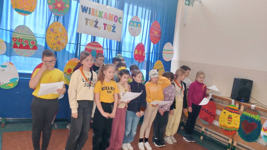 Festiwal Piosenki Wielkanocnej. 
Festiwal Piosenki Wielkanocnej. Na zdjęciu uczniowie klasy 3 b   śpiewają piosenkę, w tle duże pisanki kolorowane przez uczniów.  