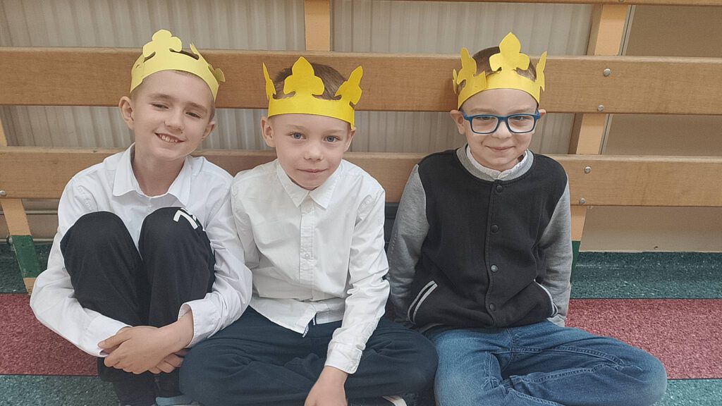 Tysiąclecie koronacji Bolesława I Chrobrego. Na zdjęciu trzech chłopców siedzących na podłodze, na głowach maja żółte korony z papieru.