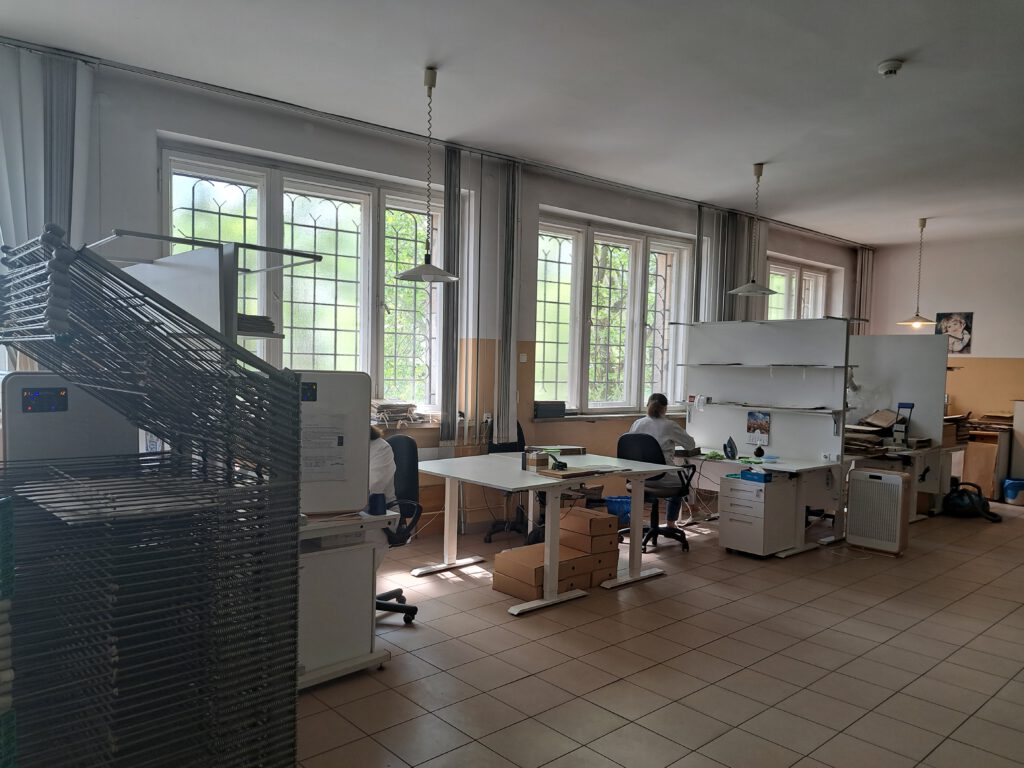 Konkurs "Bez korzeni nie zakwitniesz". Przedstawia pracownię konserwacji akt w Archuwum Państwowym we Wrocławiu. Pracownia wyposażona jest w biale biurka i regały. Znajdują się w niej również szare metalowe suszarki do suszenia akt. Podłoga w jasne kafelki, które muszą odbijać promienie słoneczne wchodzące przez duże okna.