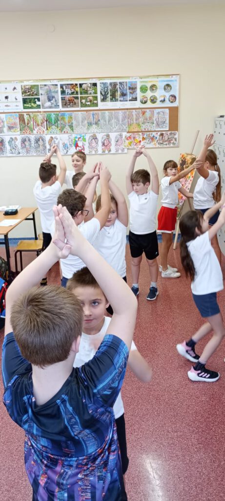Projekt Active Sister Schools. Na zdjęciu uczniowie ubrani na sportowe wykonują różne ćwiczenia, trzymają ręce w górze.