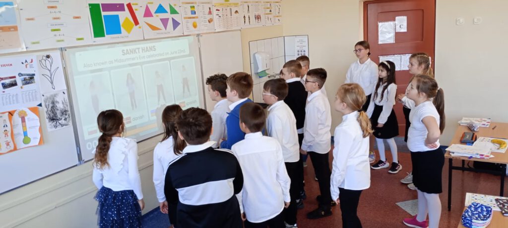 Projekt Active Sister Schools. Na zdjęciu uczniowie klasy trzeciej ubrani w strój galowy przypatrują się ćwiczeniom wyświetlanym na białej tablicy.
