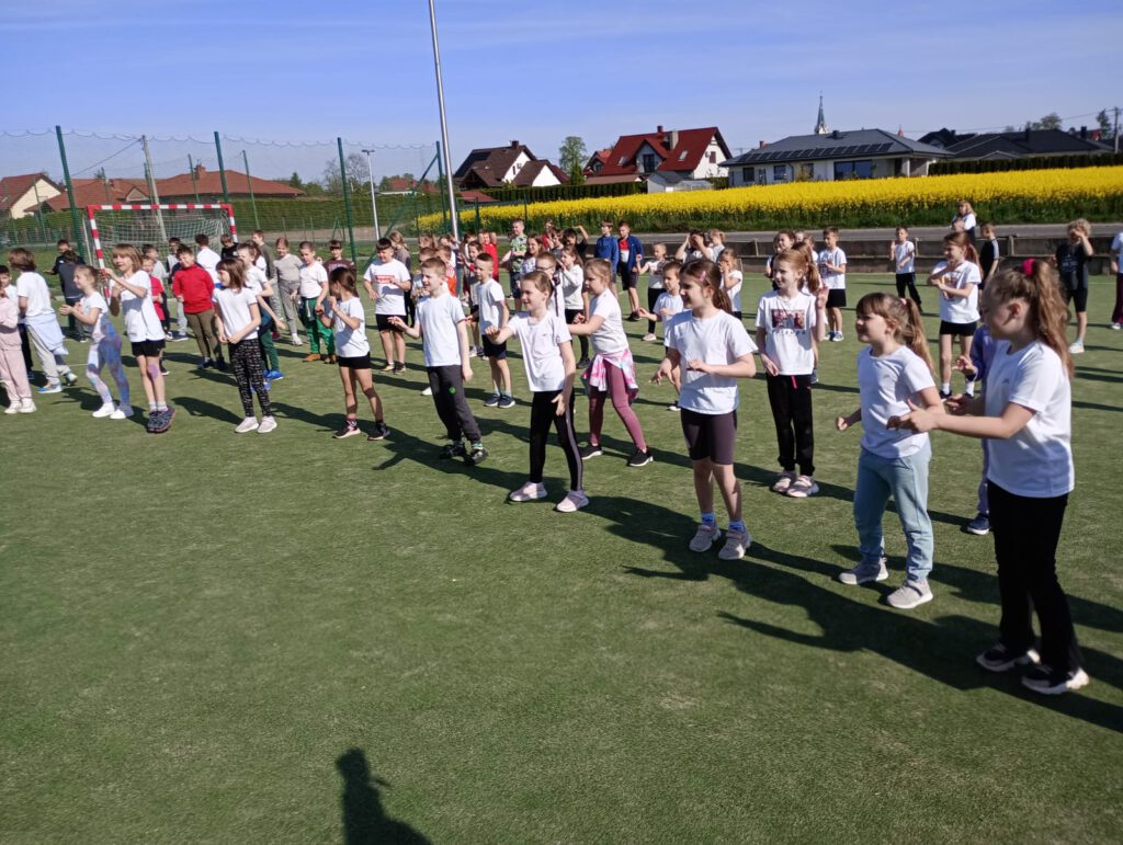 Święta Majowe. Uczniowie klas 1-3 ubrani w stroje sportowe biorą udział w rozgrzewce przed biegami.