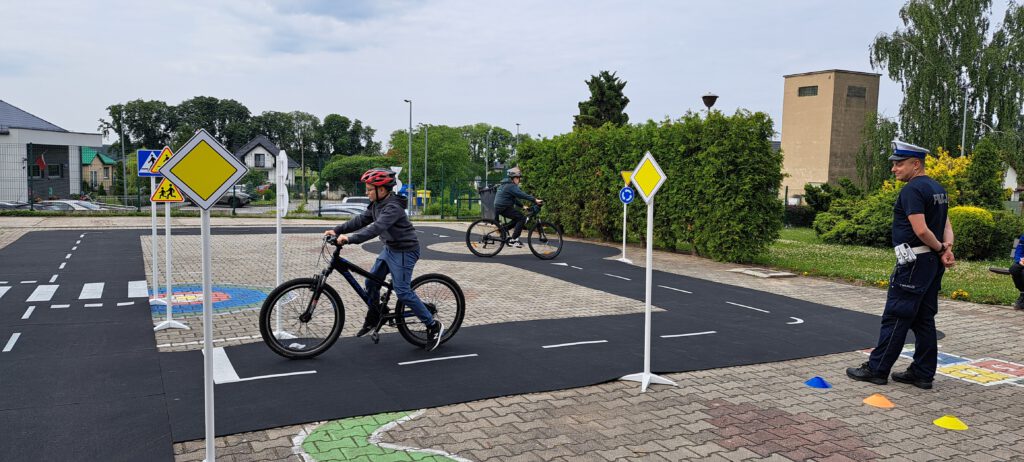 Egzamin na kartę rowerową. Na zdjęciu policjant egzaminuje dwoje uczniów jadących rowerem po wyznaczonej trasie,