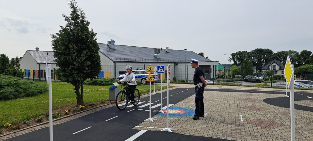 Egzamin na kartę rowerową. Na zdjęciu policjant egzaminuje uczennicę jadącą rowerem po wyznaczonej trasie,