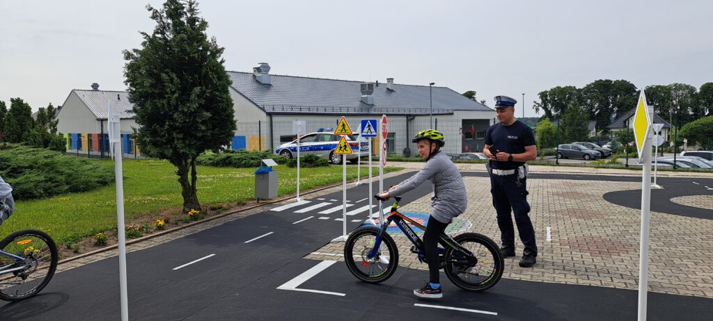 Egzamin na kartę rowerową. Na zdjęciu policjant egzaminuje uczennicę jadącą rowerem po wyznaczonej trasie,