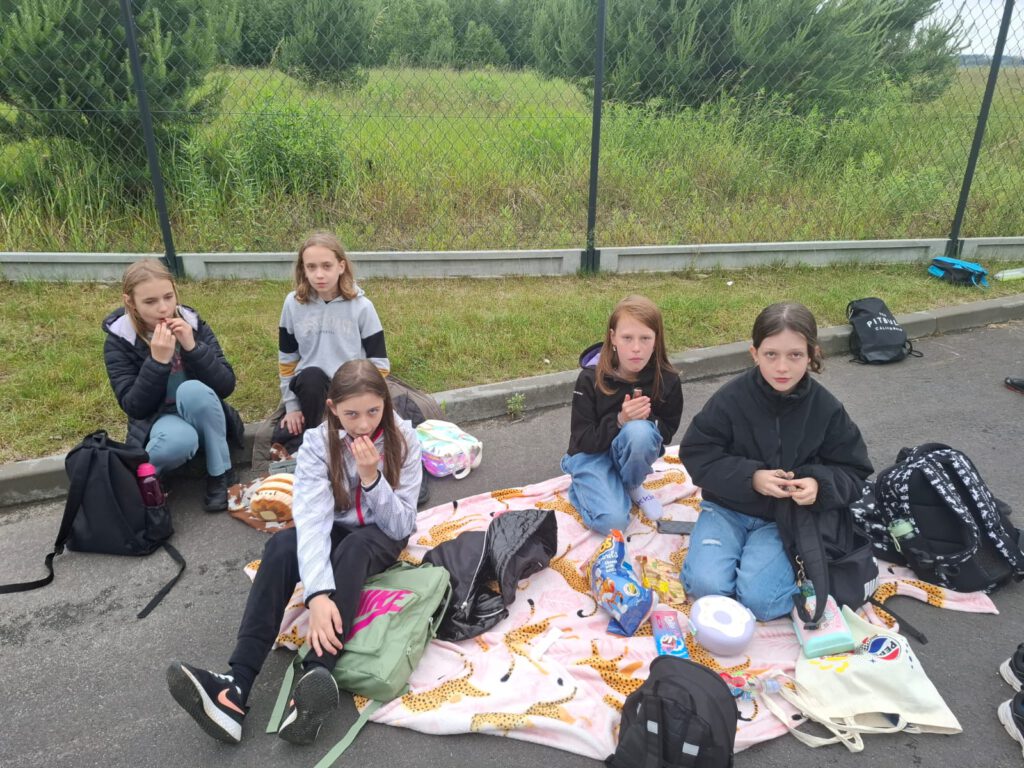 Projekt edukacyjny ,,Jestem w pSzoku”. Na zdjęciu dziewczynki siedzą na kocu i jedzą kanapki.