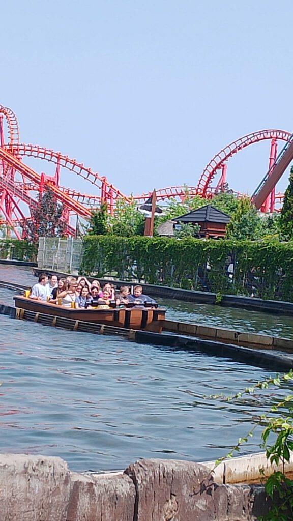 Na zdjęciu uczniowie płyną łódką po zjechaniu z wodnej zjeżdżalni. W tle rollercoastery.
