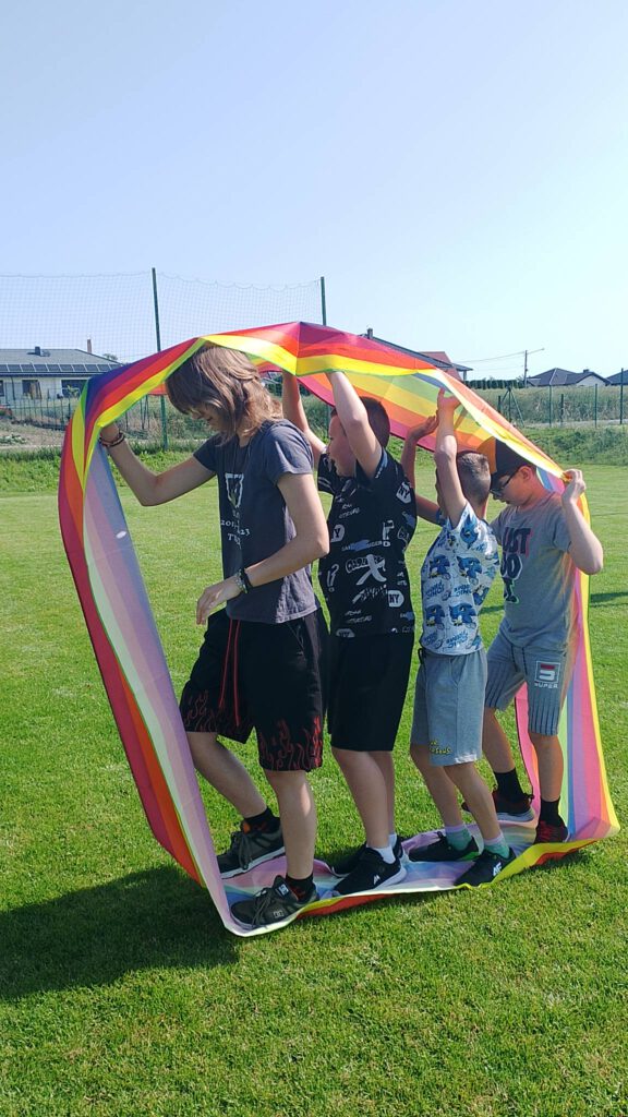 Piknik "Powitanie lata". Na zdjęciu jedna dziewczynka i czterech chłopców bierze udział w konkurencji sportowej: idąc jeden za drugim uczniowie przechodzą w dużej w szrafie przesuwając ją na sobą.