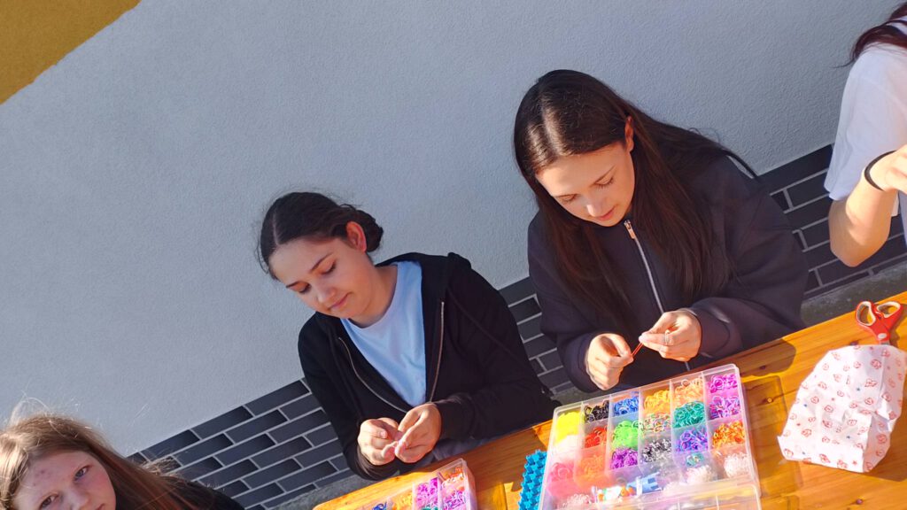 Piknik "Powitanie lata". Na zdjęciu dwie uczennice robią bransoletki z kolorowych gumeczek.