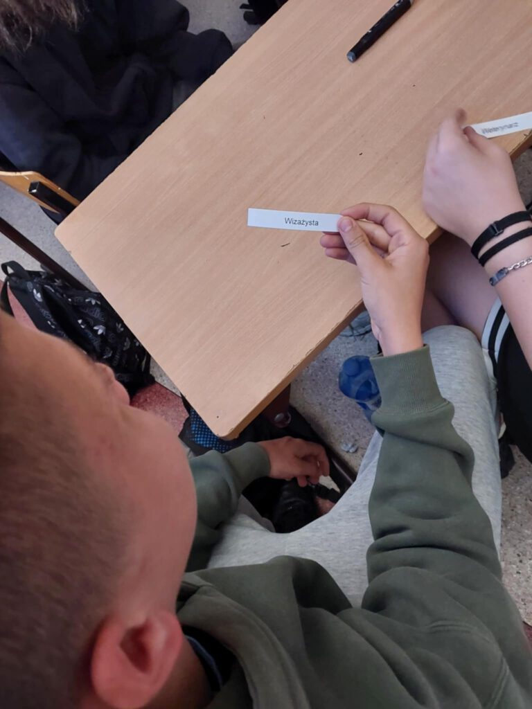 Warsztaty z doradztwa zawodowego. Na zdjęciu uczeń trzyma w ręce karteczkę z nazwą zawodu. 