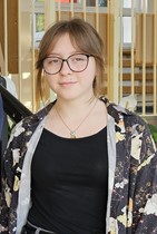Na zdjęciu uczennica klasy ósmej wyróżniona w Międzynarodowym Konkursie Matematycznym "Kangur". W tle schody i barierki przy schodach.