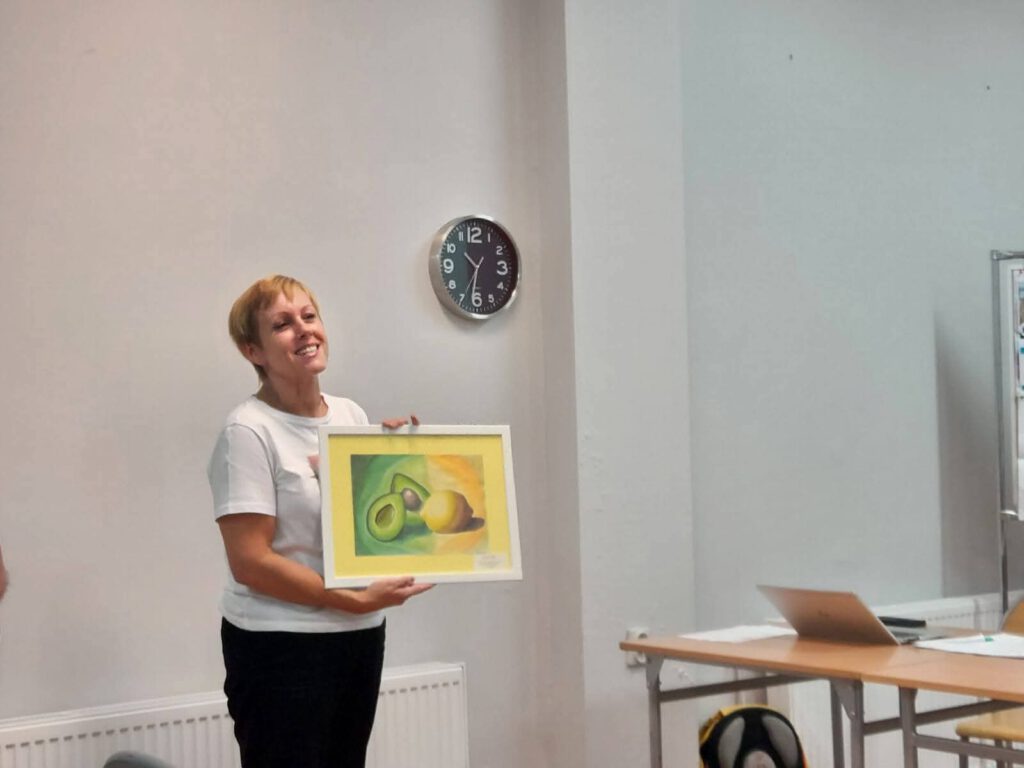 Przekazanie voucherów na wyjazd na lekcję biologii z żywymi zwierzętami. Na zdjęciu pani Dyrektor szkoły trzyma e rękach obrazek z kiwi i cytryną.