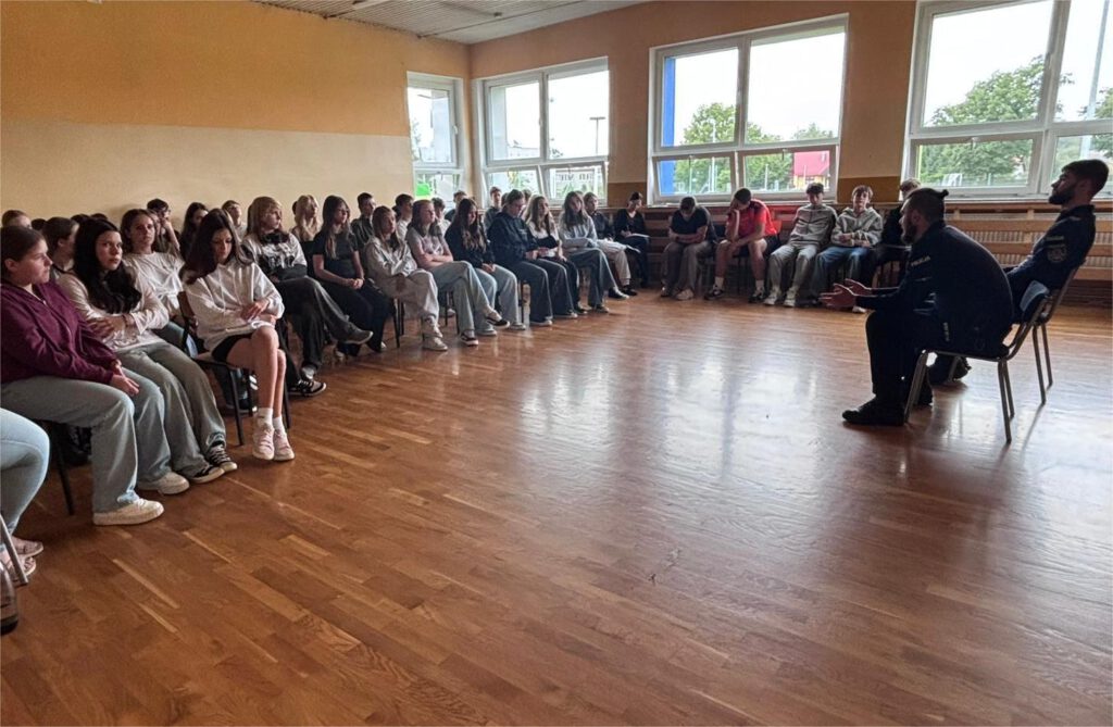 Spotkanie z policjantami na temat bezpieczeństwa. Na zdjęciu uczniowie kas 7 a, 7 b  i 8 a  siedzą  na podłodze w salce gimnastycznej i słuchają policjantów.