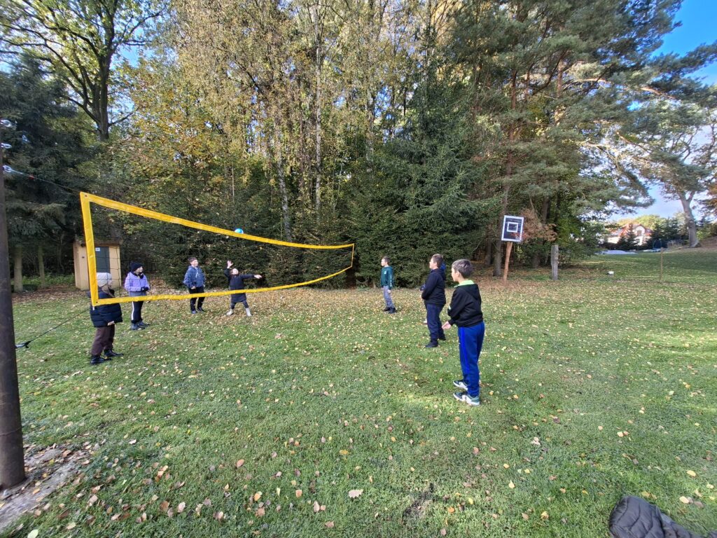 Zdjęcie przedstawia uczniów grających w siatkówkę na trawie.