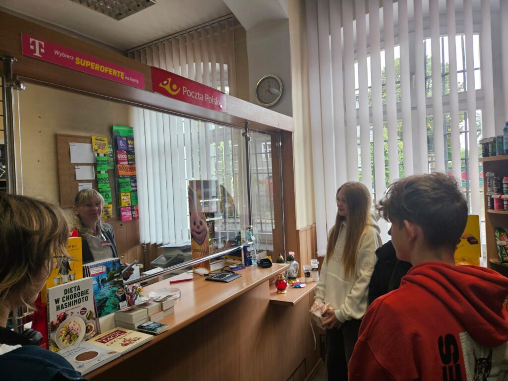 Ludzie Listy Piszą... Czyli Światowy Dzień Poczty W Naszej Szkole. Na zdjęciu widoczne okienko pocztowe w urzędzie pocztowym w Gaworzycach. Po prawej stronie stoi dwóch uczniów naszej szkoły.