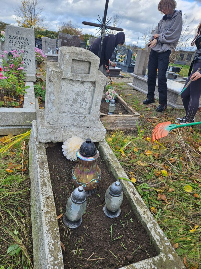 Ocalić od zapomnienia, czyli sprzątamy opuszczone groby. . Na zdjęciu widoczny duży , murowany nagrobek z krzyżem. Pomnik jest uporządkowany. Na środku stoją trzy znicze. Pod krzyżem znajduje się sztuczny kwiat.
