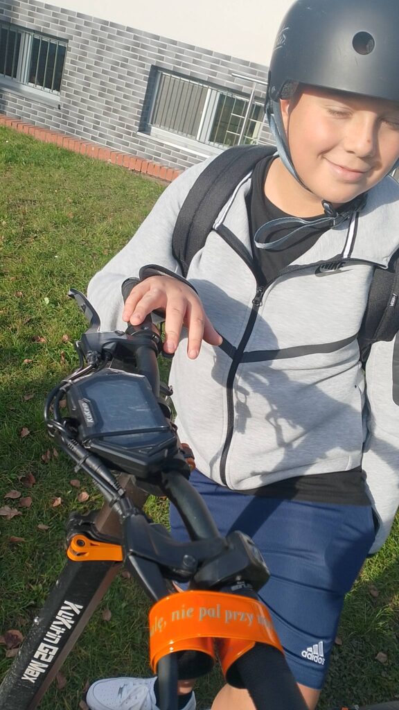 Odblaskowa Szkoła 2025. Na zdjęciu uczeń na hulajnodze w kasku pozuje do zdjęcia.