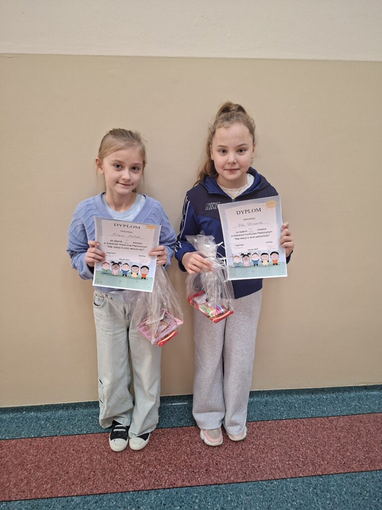 Zdjęcie przedstawia uśmiechnięte laureatki konkursu trzymające w ręce dyplomy oraz drobne upominki zapakowane w celofan.
W tle zdjęcia beżowa ściana.