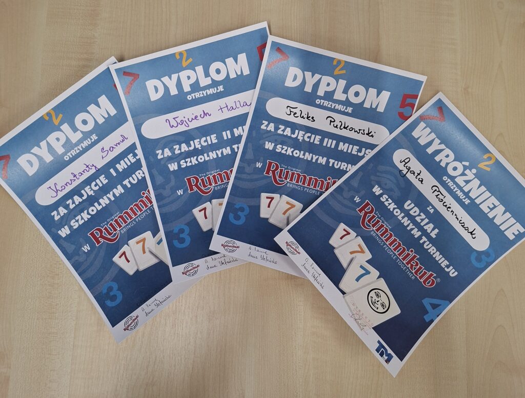 Zdjęcie przedstawia dyplomy ze Szkolnego Turnieju Rummikub. Napisy na dyplomie biało-Czerwone, tło niebieskie i kolorowe cyfry.
