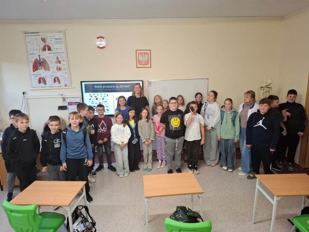 Spotkania ze specjalistami w ramach zajęć z edukacji zdrowotnej i przyrodniczej. Na zdjęciu uczniowie pozują do zdjęcia z panią dietetyk i ze szkolna pielęgniarką. W tle tablica z prezentacja na temat zdrowych produktów.