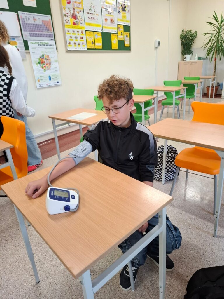 Spotkania ze specjalistami w ramach zajęć z edukacji zdrowotnej i przyrodniczej. Na zdjęciu uczeń siedzi ławce i mierzone jest mu ciśnienie.