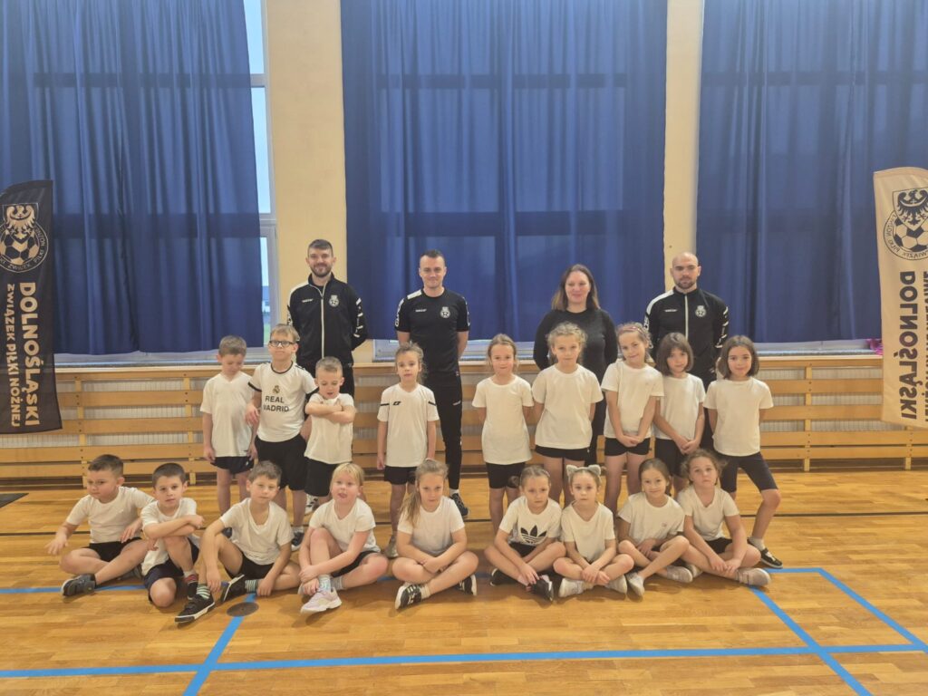 zDolnośląskie Dzieciaki. Na zdjęciu uczniowie klasy pierwszej ubrani na sportowo pozują do zdjęcia wraz z wychowawczynią trenerami piłki nożnej. 