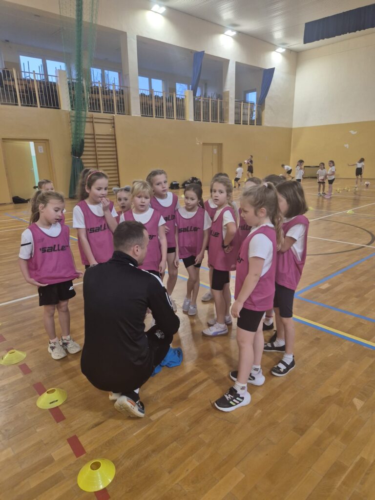 zDolnośląskie Dzieciaki. Na zdjęciu jeden z trenerów rozmawia z dziewczynkami i  podaje instrukcje do wykonania zadania. 
