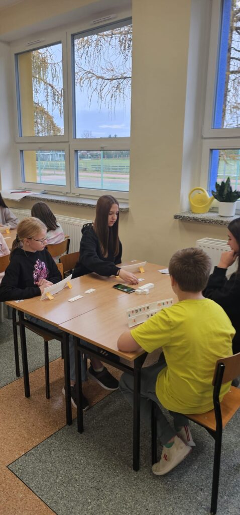  Na zdjęciu widzimy 4 uczniów (trzy dziewczynki i jeden chłopiec) przy stoliku, którzy grają w Rummikuba.