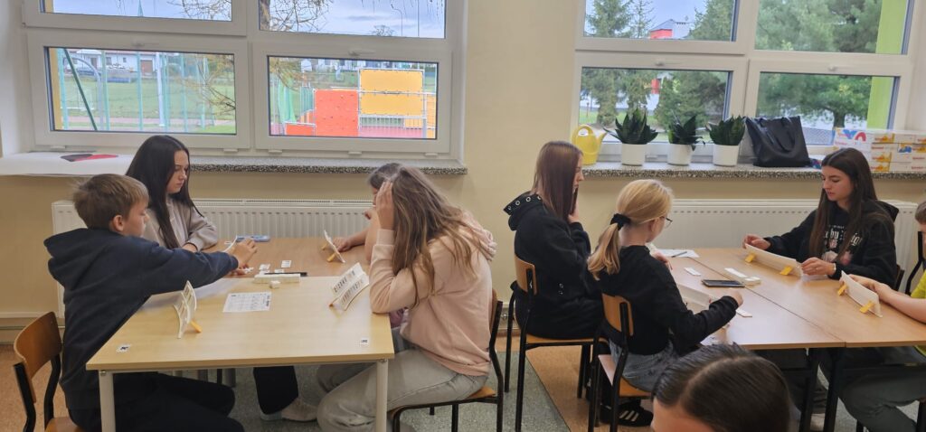 Na zdjęciu widzimy dwa stanowiska stolików, przy każdym siedzą 4 uczniów grających w Rummikuba.