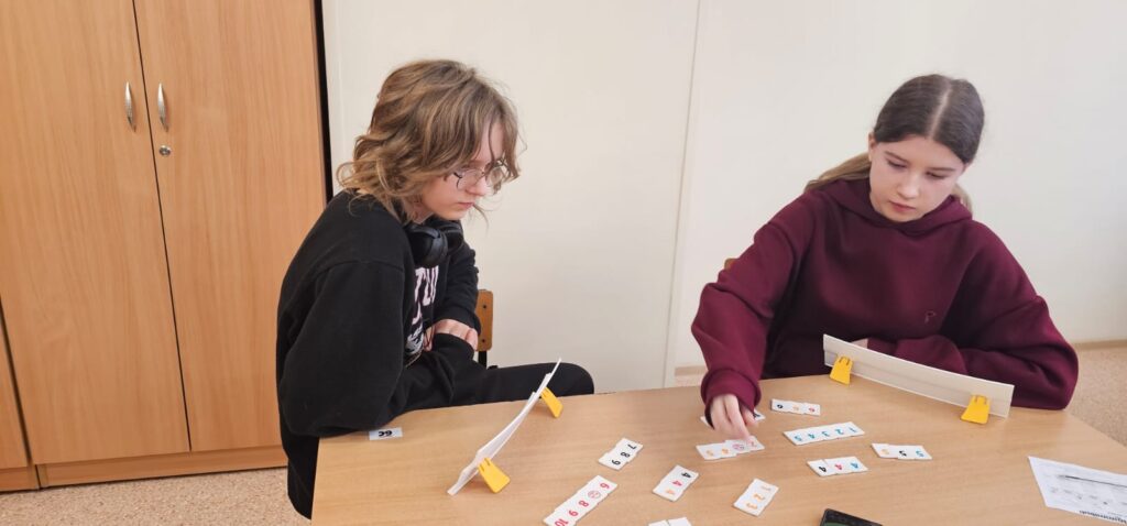  Zdjęcie przedstawia dwie uczennice, które grają w Rumikuba, układają kostki na tabliczce.