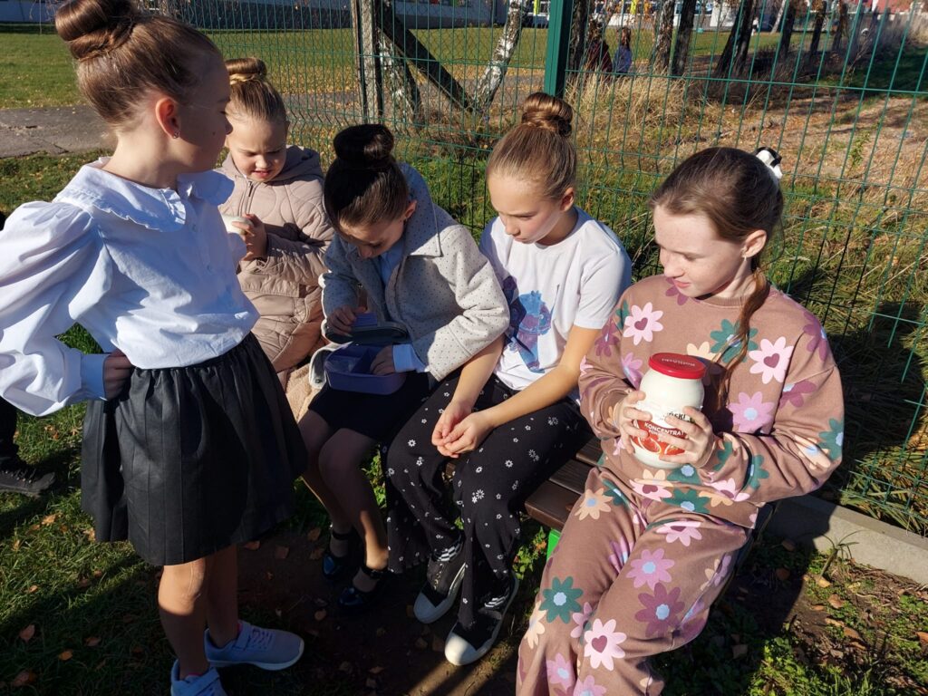 Dzieci po realizacji zadania z projektu - Podróże w czasie z "Etnoekipą" - tak się żyło dawniej na wsi. – ubijają w słoikach śmietanę i dzięki współpracy powstaje masło.