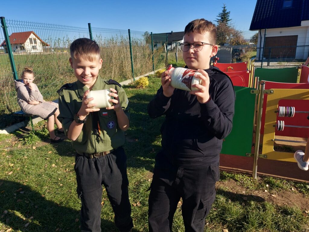 Dzieci po realizacji zadania z projektu - Podróże w czasie z "Etnoekipą" - tak się żyło dawniej na wsi. – ubijają w słoikach śmietanę i dzięki współpracy powstaje masło.