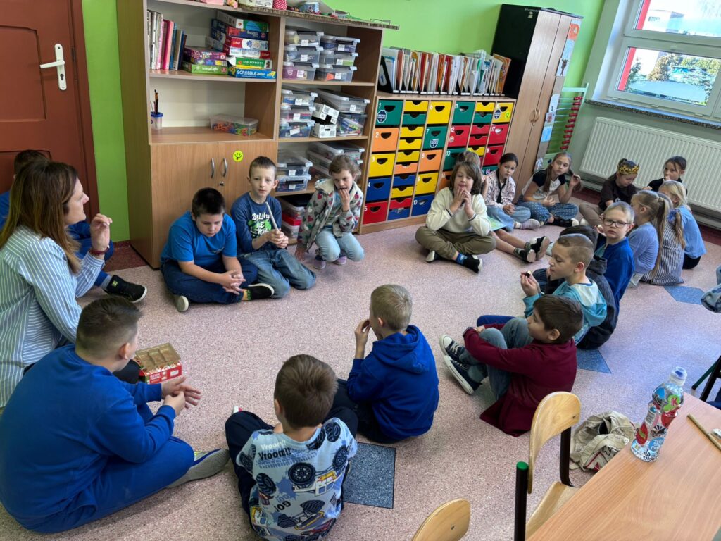 Światowy Dzień Praw Dziecka. Na zdjęciu znajduje się grupa dzieci z klasy 3b ubranych w niebieskie koszulki, leżących  i stojących razem w szkolnej przestrzeni. Wskazują na plakat informacyjny dotyczący Praw Dziecka.