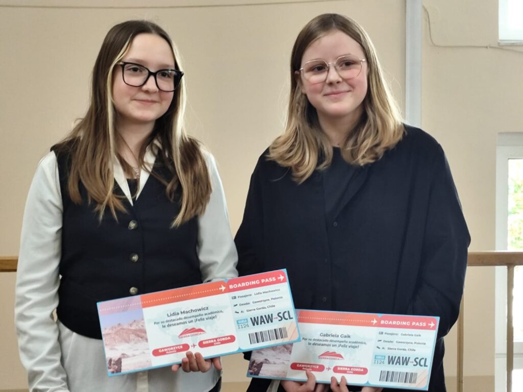 Uroczyste wręczenie biletów do Chile  na kolejną wymianę młodzieży. Na zdjęciu dwie uczennice, które otrzymały bilety, uśmiechają się i pozują do zdjęcia z biletami. 