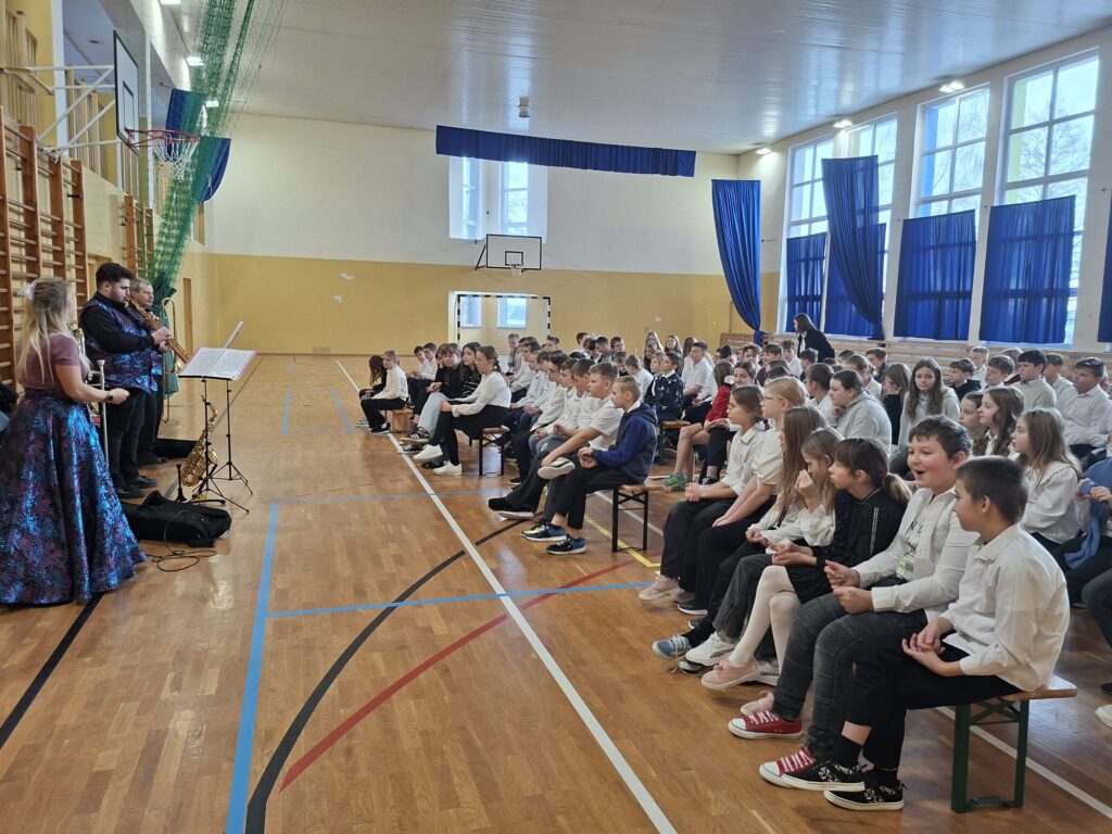 Zdjęcie pokazuje w przybliżeniu uczniów klas 4-6 siedzących na widowni w galowych strojach.