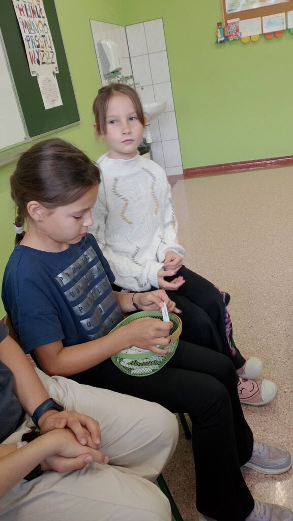 Szkolny Konkurs Literowania “Speeling Bee". Na zdjęciu uczniowie klasy trzeciej podczas konkursu. Na zdjęciu uczennica losuje słówko i literuje je w języku angielskim.